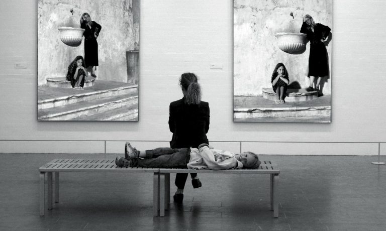 Fotografía en blanco y negro de una mujer contemplando dos cuadros de arte contemporáneo firmados
